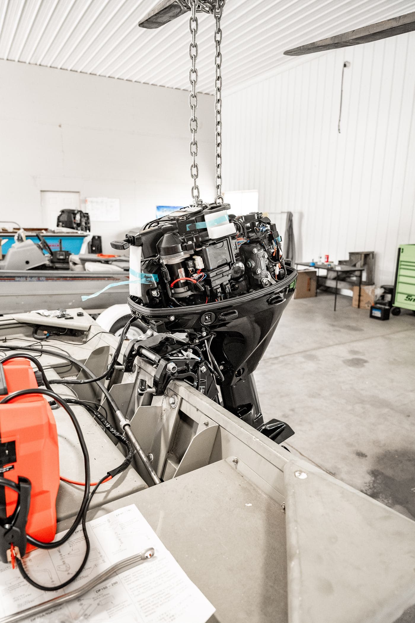 Outboard engine suspended from a chain hoist above a boat transom in the service bay
